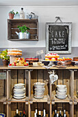 Cake counter with various cakes and pastries in front of a rustic wooden shelf