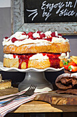 Two-tier sponge cake with cream and raspberries on a cake stand