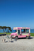 Vintage-style pink ice cream van with a small seating area by the sea