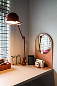 Desk with red floor lamp and oval mirror in modern office