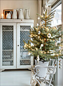 Decorated Christmas tree in an old enamel bucket, cupboard with glass doors in the background