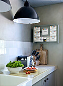 Kitchen utensils on concrete countertop with black lamps above