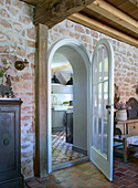 View from the living room with natural stone wall through an open arched door into the kitchen
