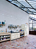 Kitchen unit made of light-coloured wood, shelves above in the conservatory