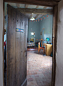 View through old wooden door into children's room with terracotta tiled floor and rustic wooden beamed ceiling