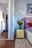 Bedside table with flower vase next to bed with upholstered headboard, rug with terrazzo pattern