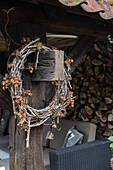 Rustic wreath on wooden pillar next to stacked firewood and rattan sofa