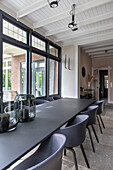 Black dining table and chairs in a bright room with large windows and ceiling beams