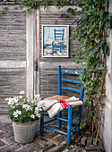 Blauer Holzstuhl und Metall-Blumentopf vor verwitterter Holzwand