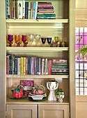 Shelves with books, colorful glasses and decorative ceramics