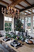 Dining table set for Christmas with chandelier, black candles and Christmas tree in the background