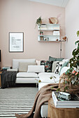 Living room with white corner sofa, wall shelves and pink wall paint