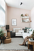Wohnzimmer mit weißem Ecksofa, Wandregalen und rosa Wandfarbe
