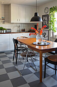 Eat-in kitchen with white cupboards, wooden table, various chairs and checkered tiles