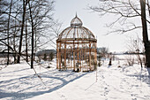 Vintage-Pavillon im verschneiten Wintergarten mit kahlen Bäumen