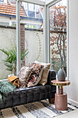 Black leather chaise with patterned pillows in front of large windows in the conservatory