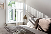 Light-flooded bedroom with bed linen in earthy tones and white curtains