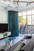 Living room with large glass front, concrete-look ceiling and blue curtains