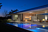 Blick über Pool in offenen Wohnraum und auf Terrasse in Abendbeleuchtung
