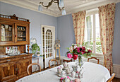 Oval table with vintage china, antique sideboard and floral curtains in the dining room