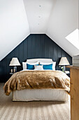 Bed with fur blanket in bedroom with sloping ceiling