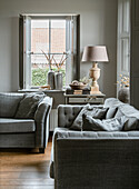 Cozy seating area with grey sofas, side table and table lamp in front of window