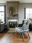 Grey armchair in front of a fireplace with wooden decorations in a living room