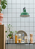 Kitchen shelf with glass containers and green wall spotlight in front of white tiled wall