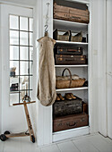 Shelf with rustic wooden boxes, vintage suitcases and wooden scooter in white hallway