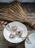 Garlic bulbs on decorative plate with fish motif and straw broom in the background