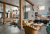 Open-plan living room with wooden beams, leather and velvet furniture and kitchen area in the background