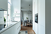 Moderne, weiße Küche mit Blick auf Essbereich und Kugel-Pendelleuchte