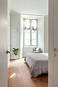 Bright bedroom with double bed, wooden floor and houseplant by the window