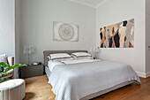 Doppelbett mit geometrischer Bettwäsche und abstraktem Wandbild