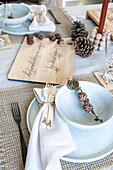 Set dining table with light blue plates, wooden board with lettering and pine cone decoration