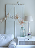 White living room with dried flowers in glass vase and table lamp