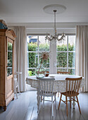 Dining room with round table, wooden furniture and chandelier in front of large windows