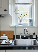 Kitchen unit with stainless steel sink, nostalgic taps and glass vase in front of window