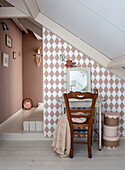 Desk with wooden chair in front of wallpaper with diamond pattern under sloped ceiling