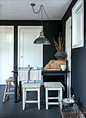 Dining area with black walls, rustic stools and industrial-style pendant light