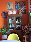 Display cabinet with figurines and masks, surrounded by colourful artwork and plants