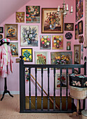 Staircase with black banister, pink wall and numerous flower pictures