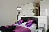 Schlafzimmer mit Doppelbett mit lila Farbakzenten und weißen Schränken