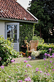 Small seating area with rattan armchair and flower pots in the garden in front of a green house