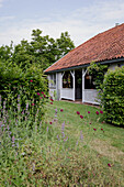 Einfamilienhaus mit Veranda, umgeben von üppigem Garten und blühenden Stauden