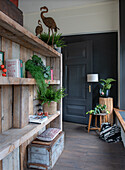 Wooden shelf with plants and vintage decorative items in rustic hallway with black door