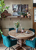 Round wooden table with green velvet chairs and bouquet of flowers in the dining room