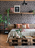 Bedroom with brick wall, pallet bed and plants as decoration