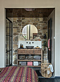 Rustic bathroom with stone wall, stone sink and round mirror