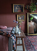 Bedroom with dark red wall, oil paintings and wooden bench at foot of bed